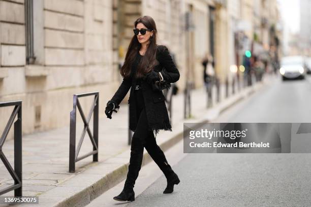 Sylvia Haghjoo wears black sunglasses from Céline, gold earrings, a black t-shirt, a black tweed ripped long jacket / coat from Chanel, black suede...