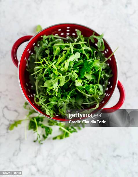 fresh arugula in a colander on white background - rucola stock-fotos und bilder