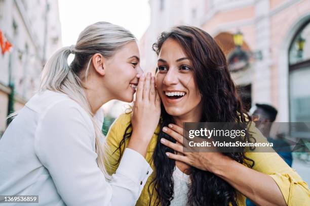 two female young friends sitting in city cafe and gossiping. - fluisteren stockfoto's en -beelden