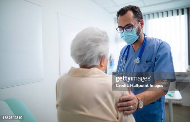 rear view of senior woman with doctor wearing protective face masks and talking warmly in doctor's office. - face mask stock-fotos und bilder