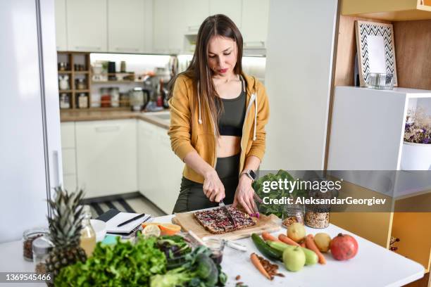 ajuste femenino cortando pastel de avena en pedazos para el almuerzo en la cocina - ropa de deporte fotografías e imágenes de stock