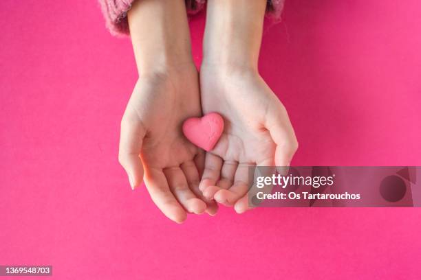 hands holding a pink candy heart on a pink background - central fotografías e imágenes de stock