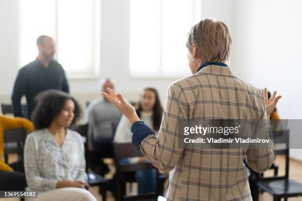 a woman is talking to a class of people sitting in chairs - employee welfare stockfoto's en -beelden