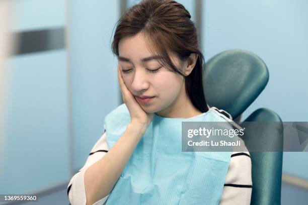 the female patient covered her mouth in pain in the dental clinic - tandfyllning bildbanksfoton och bilder