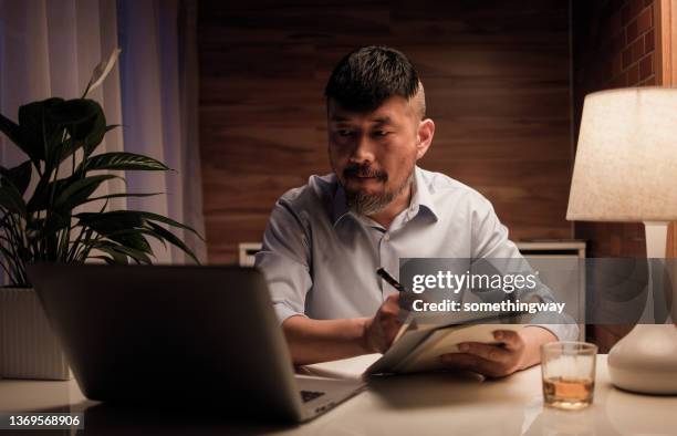 middle-aged man taking notes while having a video conference - angle poise lamp stock pictures, royalty-free photos & images