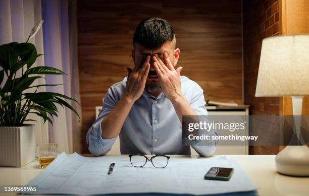 tired middle-aged designer revising plans at home - man rubbing eyes stock pictures, royalty-free photos & images