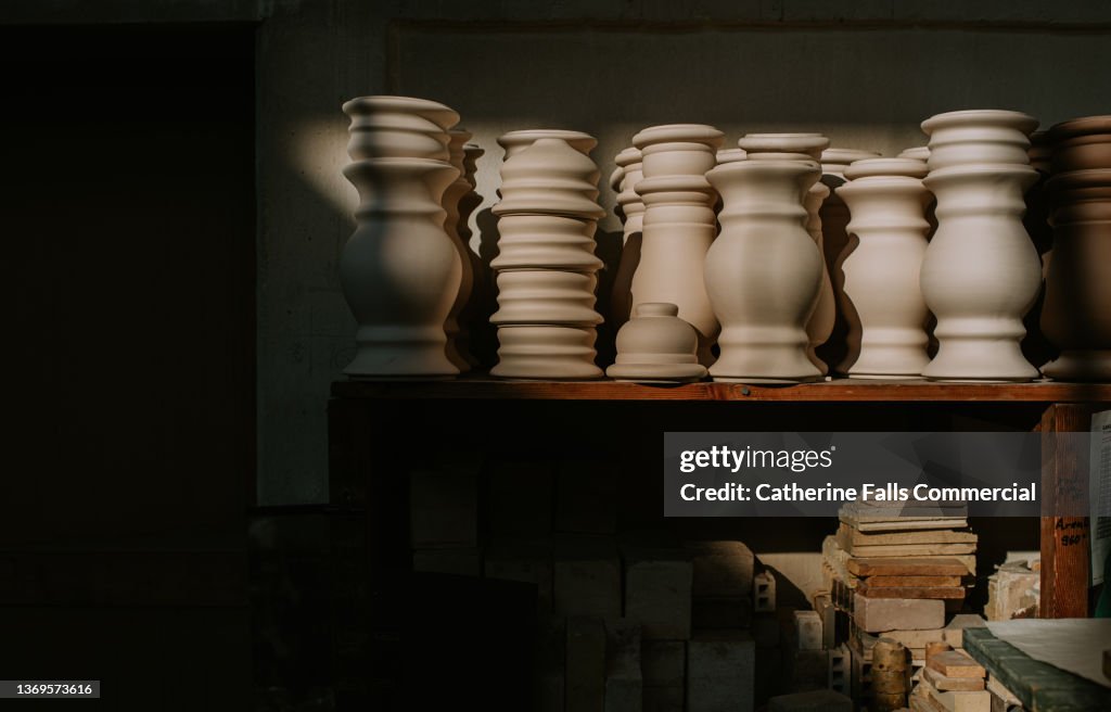 Various shaped, unglazed vases / urns sit in a row, illuminated in sunlight