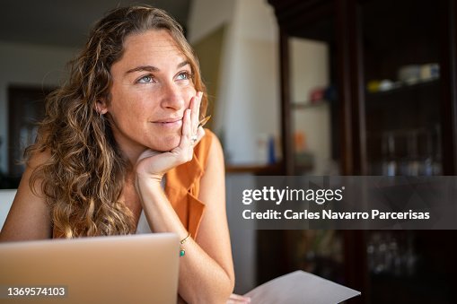 A woman with a dreamy expression working with a laptop from home A woman with a dreamy expression working with a laptop from home