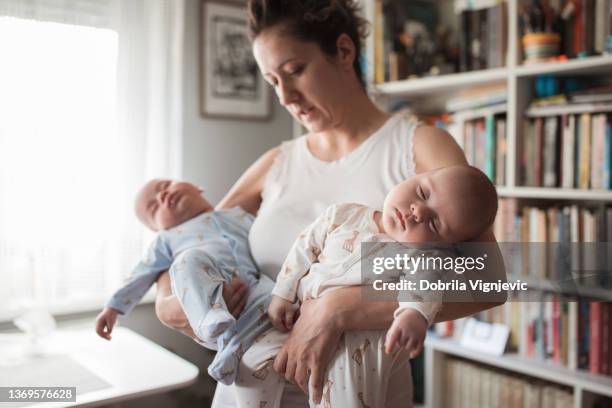 young woman holding her newborn twin babies in her arms - tweeling stockfoto's en -beelden