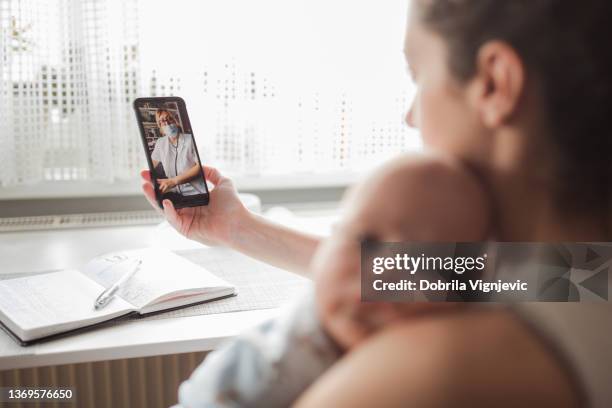 mutter hält neugeborenes und hat einen videoanruf mit einem kinderarzt - doctor using smartphone stock-fotos und bilder