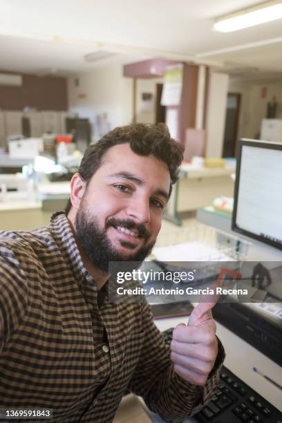 smiling bearded man in office takes self-portrait smiling happily looking at camera at his workplace - selfie male stock pictures, royalty-free photos & images