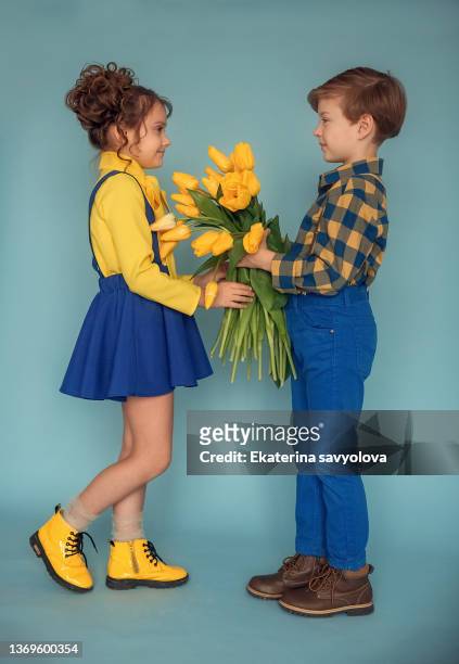 the boy got down on one knee and gives the girl a bouquet of yellow tulips. - baby boy and girl stock pictures, royalty-free photos & images