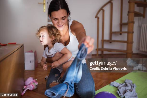 glückliche junge mutter, die ihr kleinkind zu hause auszieht - toddler mess stock-fotos und bilder