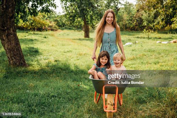 young mother playing with kids on a wheelbarrow - 2021 a funny thing 個照片及圖片檔