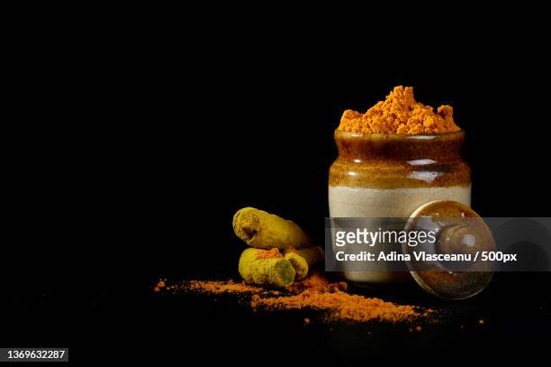 turmeric powder in clay pot with roots or barks on black background - currypulver stock-fotos und bilder