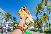 POV Point of view shot of a young travel male enjoying his vacations while eating a cuban sandwich in front of Ocean Drive, South Beach, Miami Beach, Miami, South Florida, United States of America.