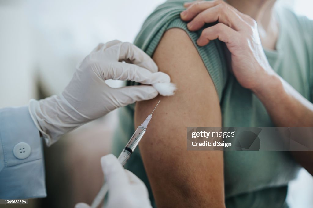 Close up of senior Asian woman getting Covid-19 vaccine in arm for Coronavirus immunization by a doctor at hospital. Elderly healthcare and illness prevention concept