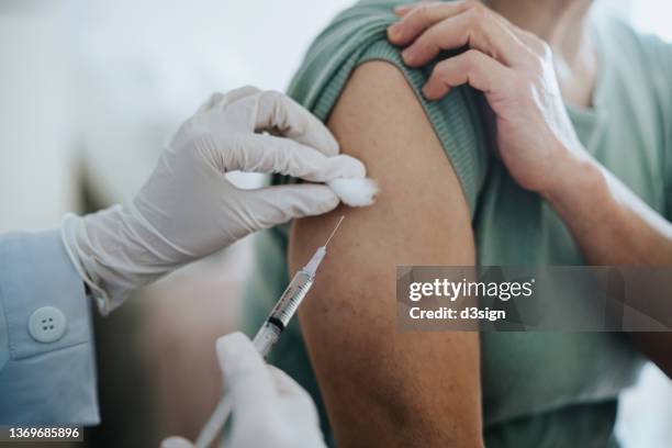 close up of senior asian woman getting covid-19 vaccine in arm for coronavirus immunization by a doctor at hospital. elderly healthcare and illness prevention concept - vaccine fotografías e imágenes de stock