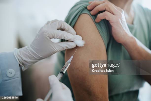 close up of senior asian woman getting covid-19 vaccine in arm for coronavirus immunization by a doctor at hospital. elderly healthcare and illness prevention concept - spuiten injecteren stockfoto's en -beelden