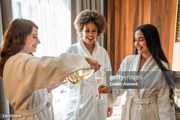 excited mixed race friends celebrating with champagne and having fun in a hotel room - spa stockfoto's en -beelden