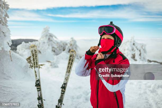 uma jovem atraente de fato de esqui está usando um capacete. no fundo das montanhas cobertas de neve - fato vermelho - fotografias e filmes do acervo