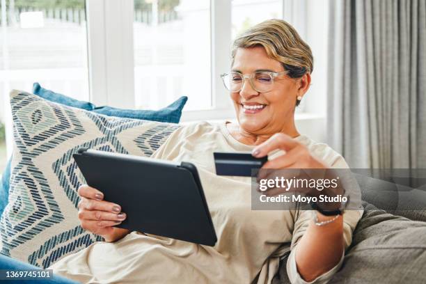 shot of a mature woman using a digital tablet and credit card at home - debt free stock pictures, royalty-free photos & images