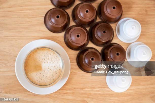 a cup of latte coffee with group of coffee capsule (or pods) on wooden table. - coffee capsules stock-fotos und bilder