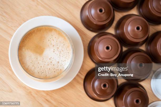 a cup of latte coffee with group of coffee capsule (or pods) on wooden table. - coffee capsules stock-fotos und bilder
