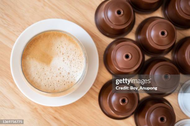 a cup of latte coffee with group of coffee capsule (or pods) on wooden table. - coffee capsule stock pictures, royalty-free photos & images