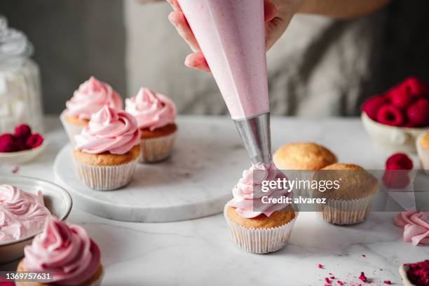 frau macht sahnehäubchen auf cupcakes mit rosa schlagsahne - sahne stock-fotos und bilder
