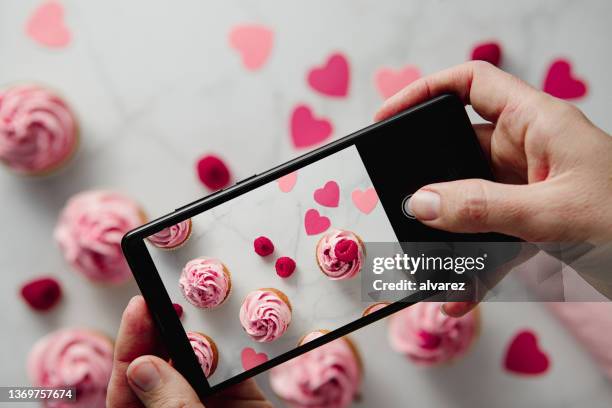 woman photographing raspberry cupcakes with paper hearts on table - cupcake stock pictures, royalty-free photos & images