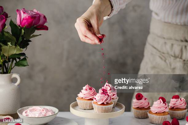woman making raspberry cupcakes in kitchen - sprinkling imagens e fotografias de stock