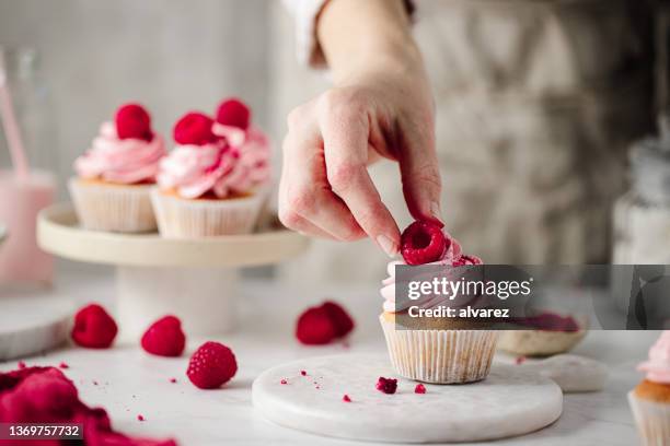 woman preparing delicious raspberry cupcakes - pasteleiro imagens e fotografias de stock