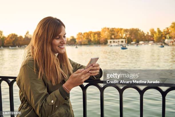 smiling woman using smartphone on embankment - one embankment stock-fotos und bilder