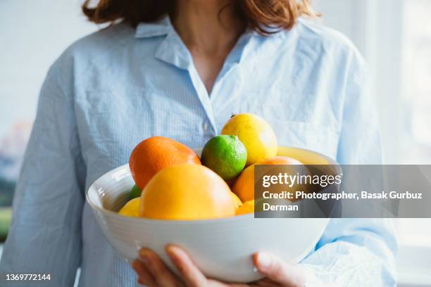 an unrecognizable woman holding a bowl full of citrus fruits; clementines, tangerines, grapefruits, lemons, limes. - vitamine c stockfoto's en -beelden