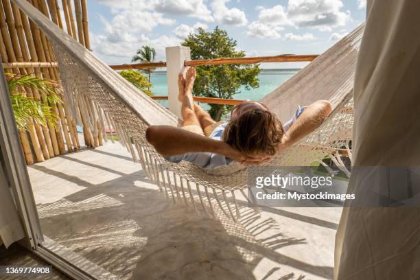 young man relaxing in an hammock on a balcony - beach balcony stock pictures, royalty-free photos & images