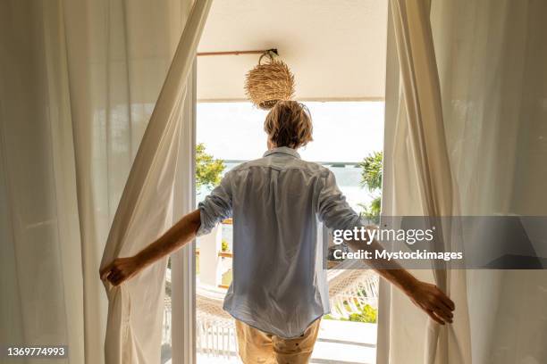 l’homme ouvre des rideaux dans la chambre au lever du soleil révélant la vue spectaculaire, le lac et le jardin - see through photos et images de collection