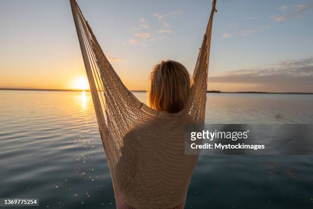 woman relaxing in a hanging chair watching sunrise on the lake - hanging chair stock pictures, royalty-free photos & images
