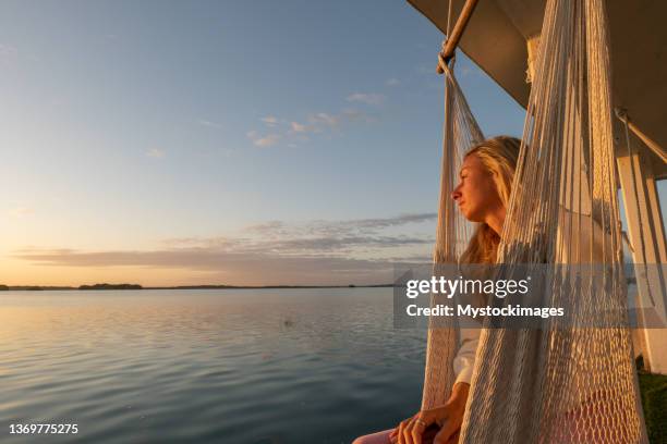 woman relaxing in a hanging chair watching sunrise on the lake - hanging chair stock pictures, royalty-free photos & images