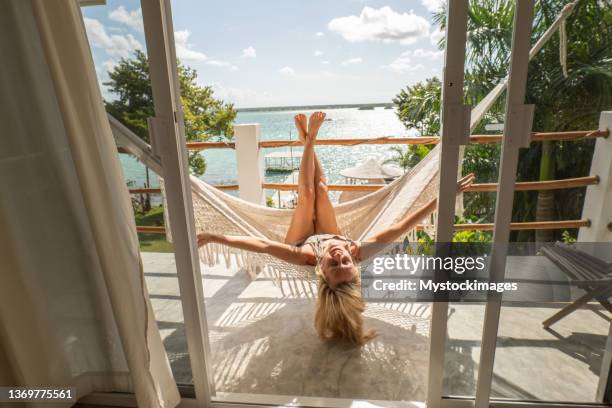 woman relaxing in an hammock on her balcony, lake and garden view - beach balcony stock pictures, royalty-free photos & images