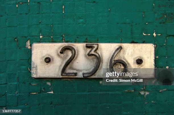 number 236 street address in raised tarnished metal numerals on a silver metal plate on a tiled building exterior with peeling dark green paint - house number stock pictures, royalty-free photos & images