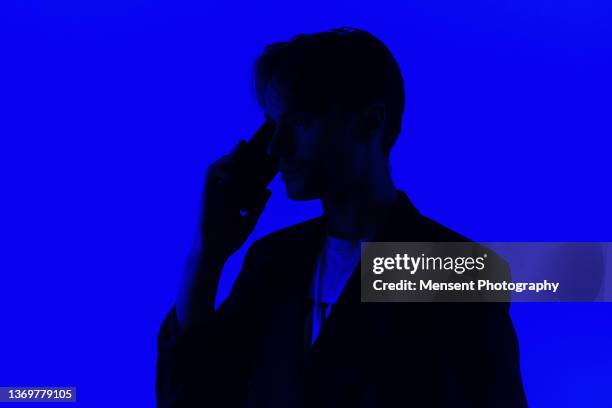 silhouette of a young man  with a mobile phone in silhouette on a blue glowing background - persona irriconoscibile foto e immagini stock