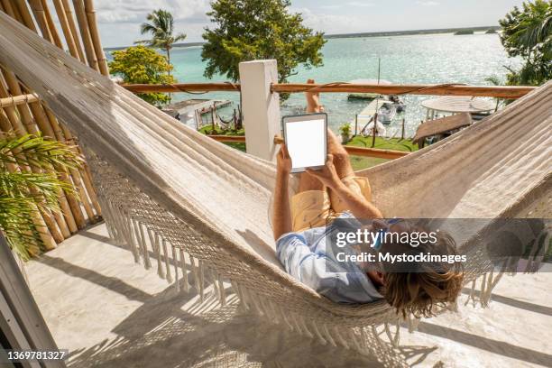 young man relaxing in an hammock on a balcony using a digital tablet - the weekend in news around the world bildbanksfoton och bilder