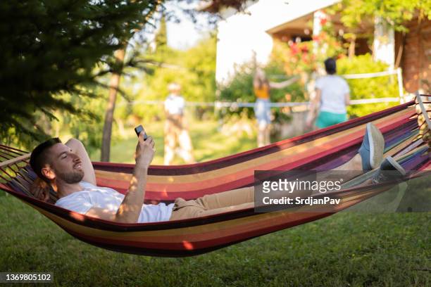 man, lying in the hammock, and using mobile phone - backyard hammock stock pictures, royalty-free photos & images