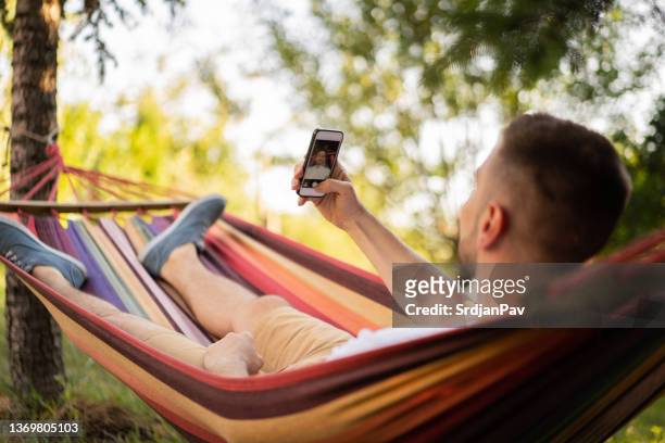 man taking selfie with mobile phone while lying in the hammock - backyard hammock stock pictures, royalty-free photos & images