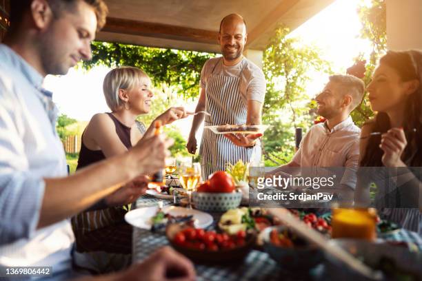 party host a chef, serving to his friends a bbq, during summer brunch - party host stock pictures, royalty-free photos & images
