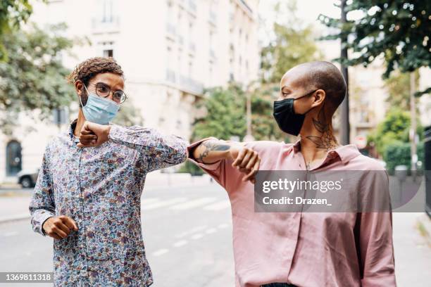 friends doing elbow bump while wearing face masks on the street - elbow greeting stock pictures, royalty-free photos & images