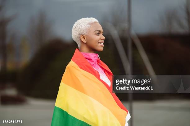 smiling lgbtqia woman wrapped in rainbow flag - democratie stock-fotos und bilder