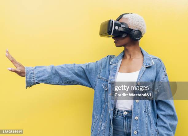 young woman with virtual reality headset against yellow background - gesticulando - fotografias e filmes do acervo