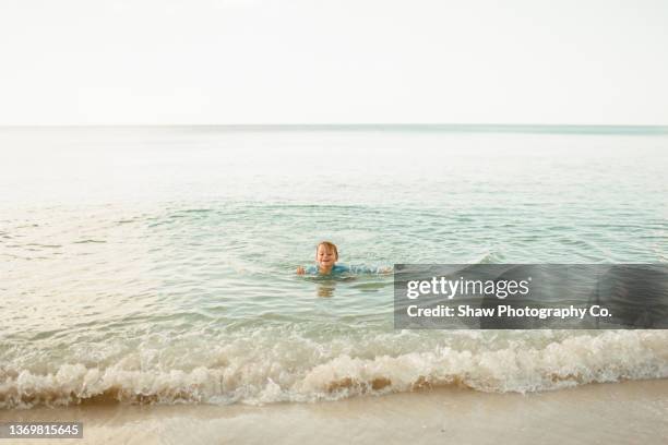 little toddler redheaded 2.5-year-old boy swimming in the ocean/bay water having the time of his life smiling with the clear horizon behind him and waves crashing in - naples florida stock-fotos und bilder